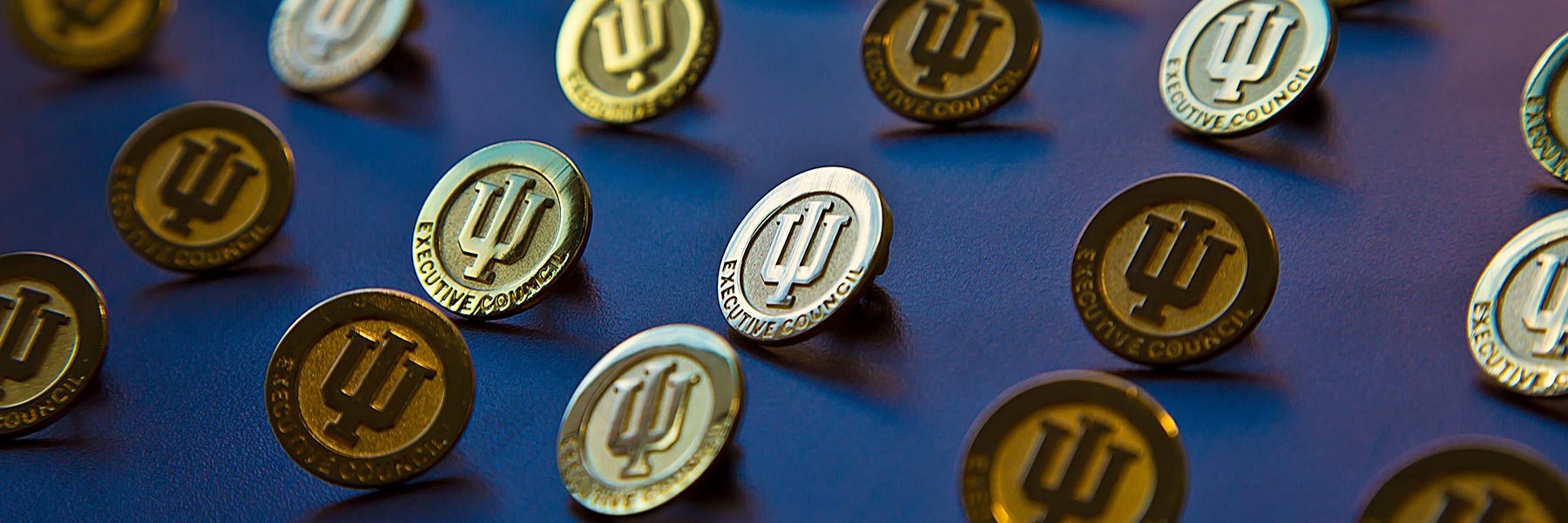 Gold IU Executive Council pins on a blue background