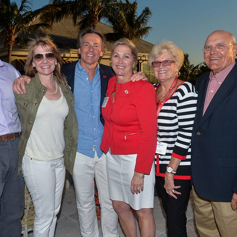 A group of people stand side by side in front of palm trees, smiling at the camera