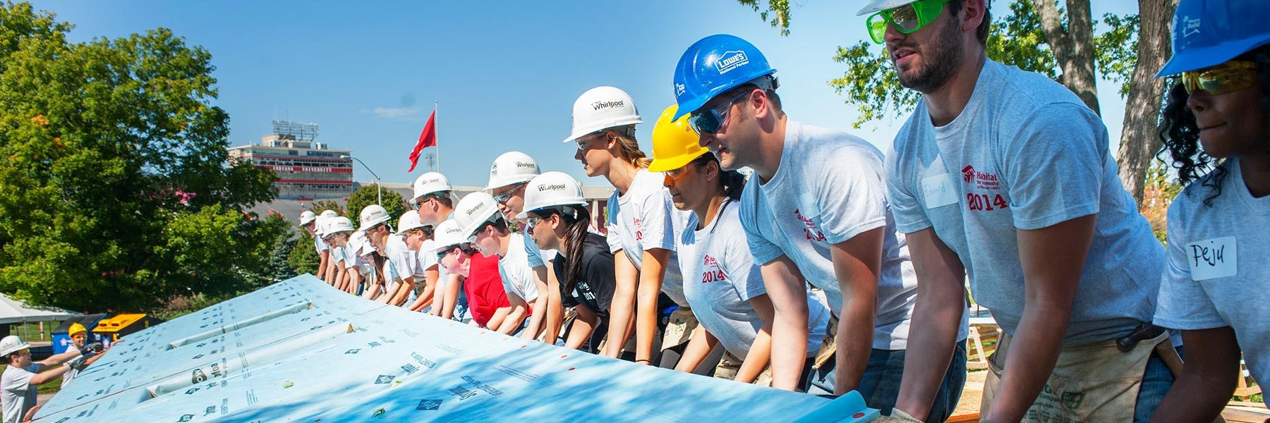 A group of people wearing hard hats work together to raise a blue wall 