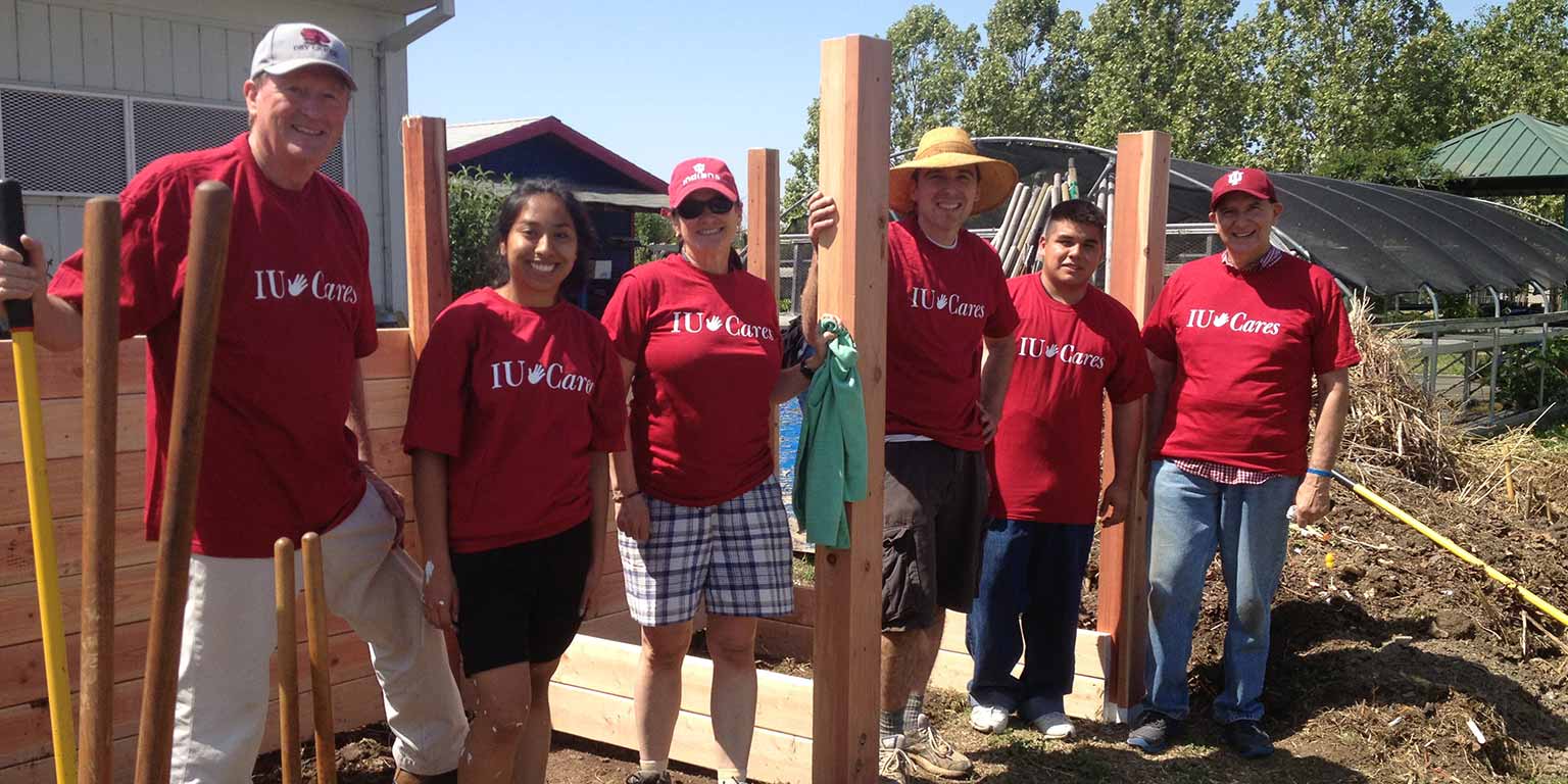 A group of people wearing IU Cares shirts stand on a wooden platform smiling at the camera